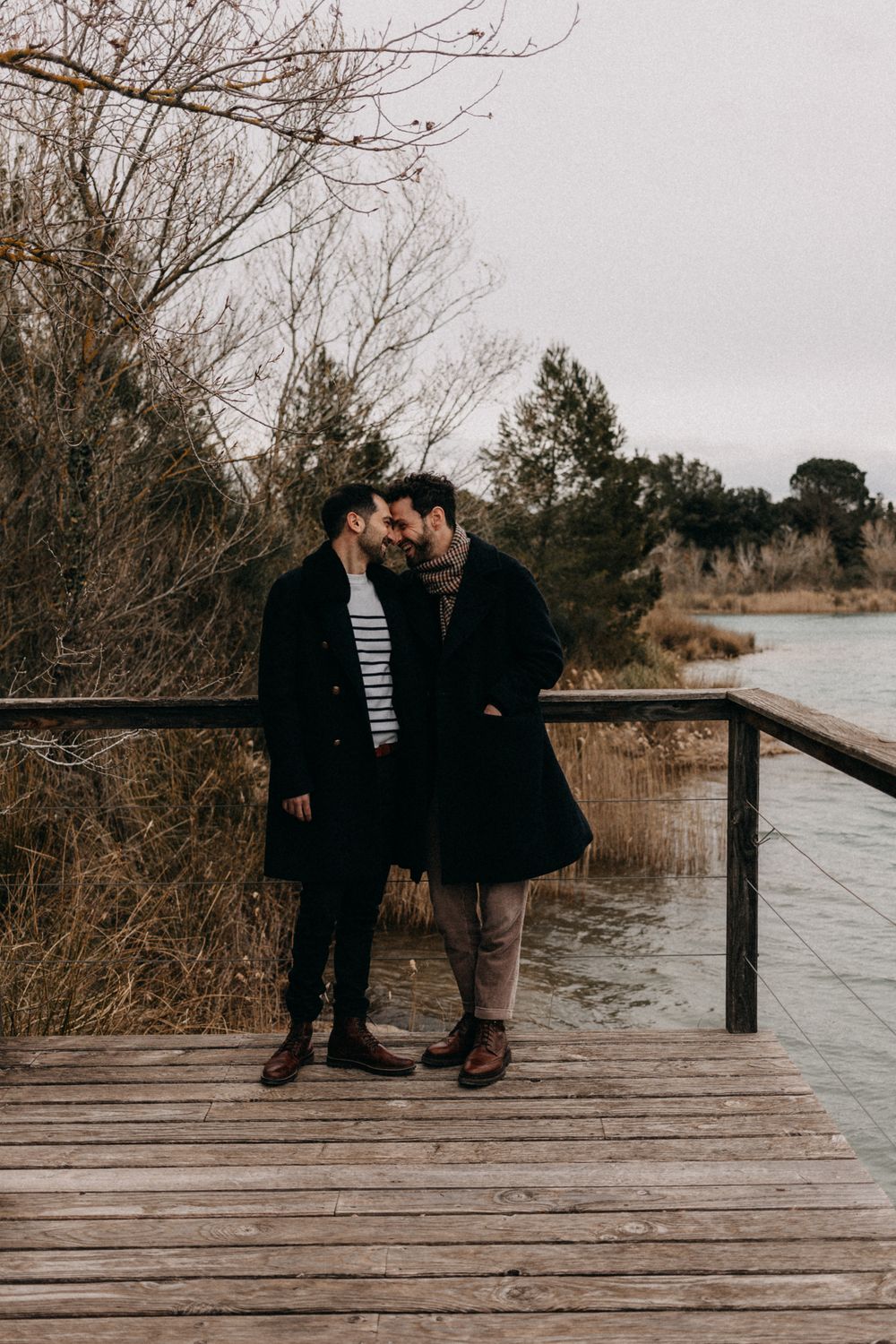 A couple shares an intimate moment on a wooden boardwalk overlooking a lake on a moody winter day.