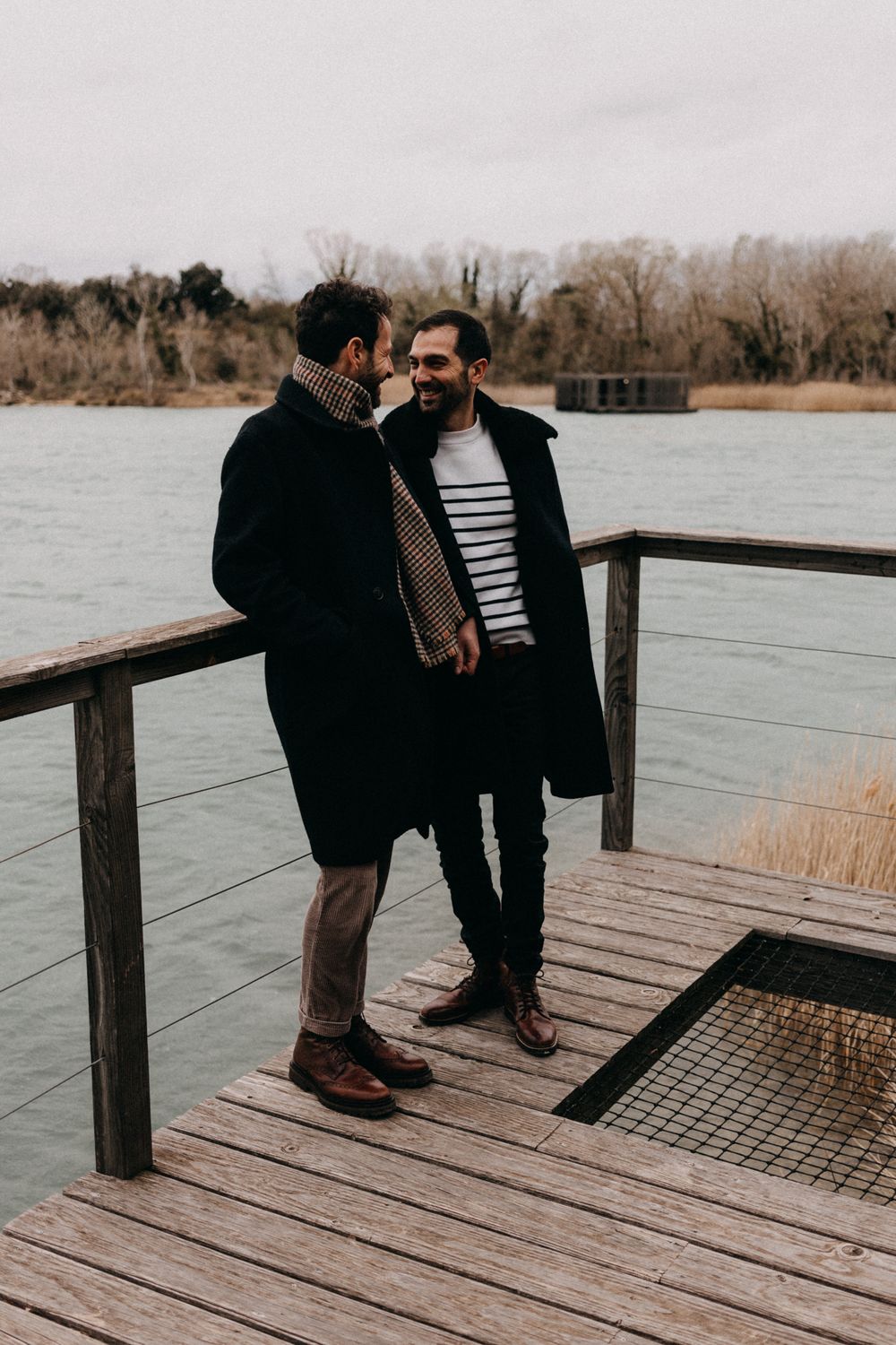 Two people share a tender moment on a wooden dock overlooking a serene lake during winter.