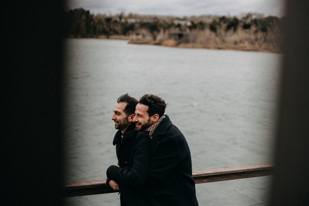Two people in dark winter coats stand close together on a boat deck overlooking misty waters.
