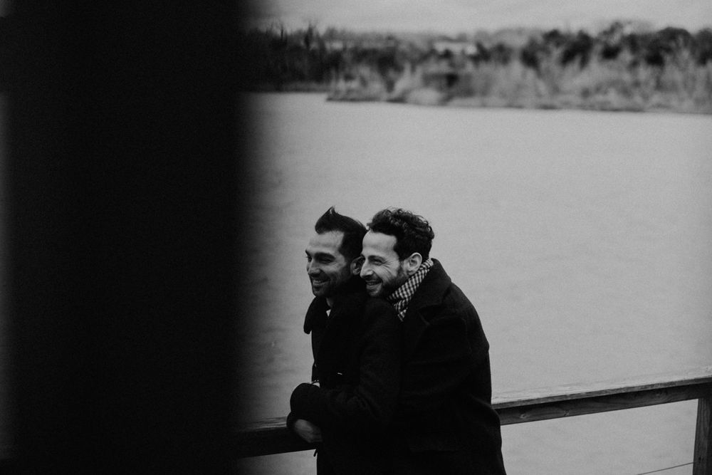 A moody black and white photograph of two people embracing on a waterfront deck.