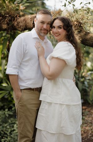 A couple wearing coordinated white outfits embrace and laugh together during an outdoor photoshoot.