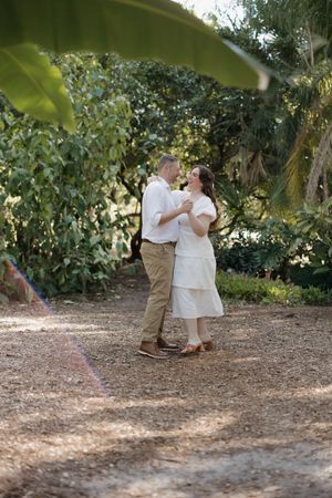 A couple shares an intimate dance moment together on a garden path surrounded by lush greenery and trees.