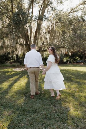 A couple sits together on a wooden swing in a serene garden setting with Spanish moss draped trees in the background.