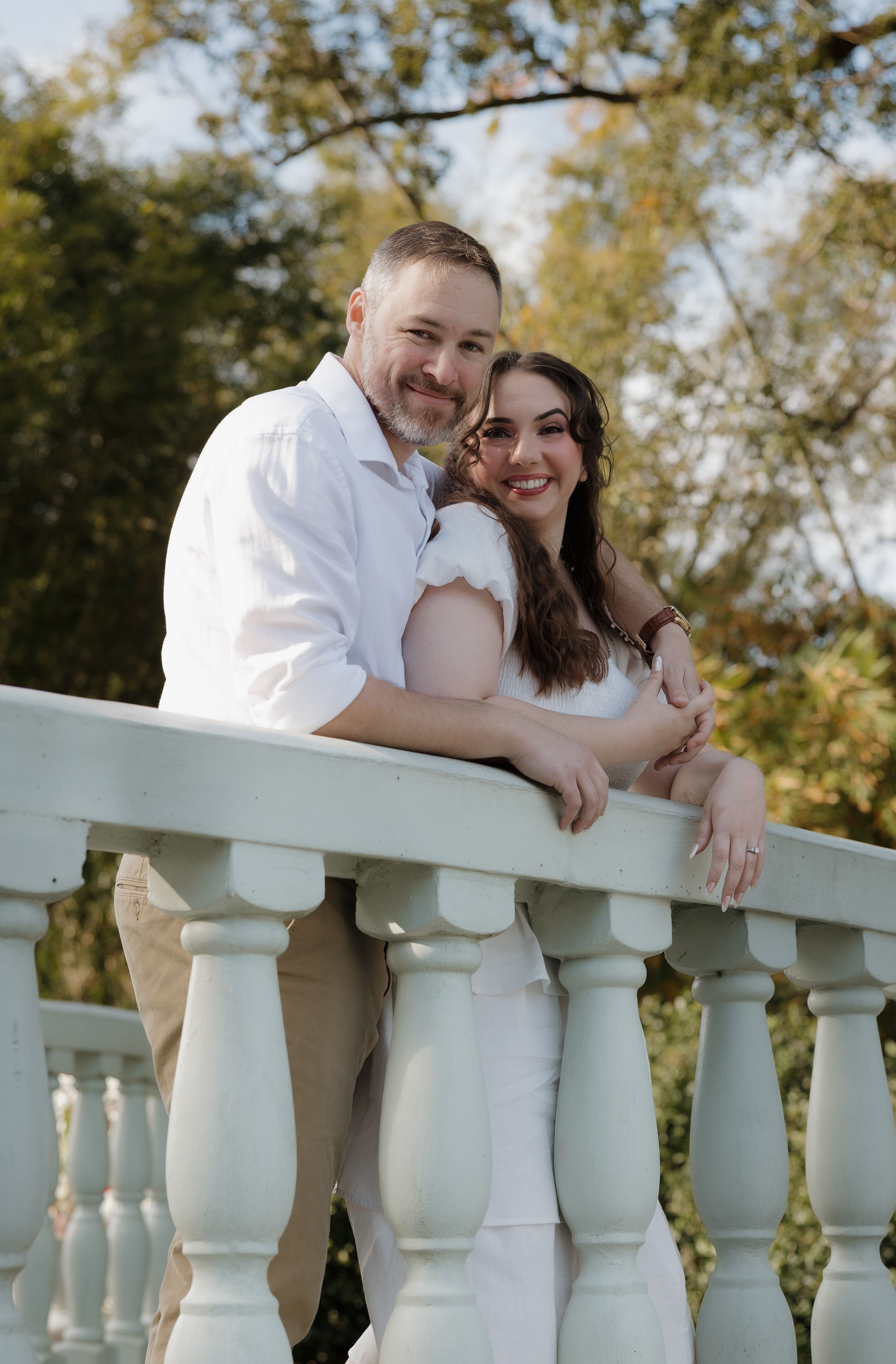 A couple in matching white outfits share romantic moments along a white balustrade railing outdoors.