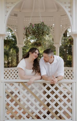 Romantic couple shares tender moments in a white gazebo with lattice details during an engagement photo session.