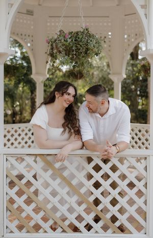 A couple shares a tender moment together in a white gazebo with lattice details on a sunny day.
