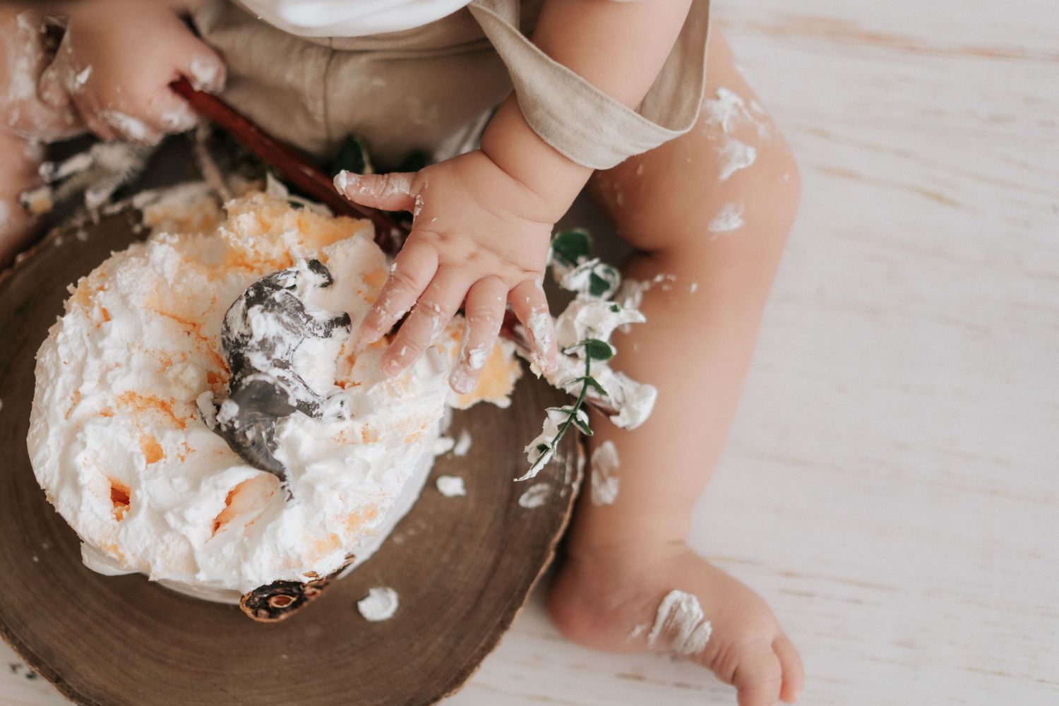 Small hands touch and play with fluffy white whipped cream or frosting on a wooden surface in a messy, playful manner.