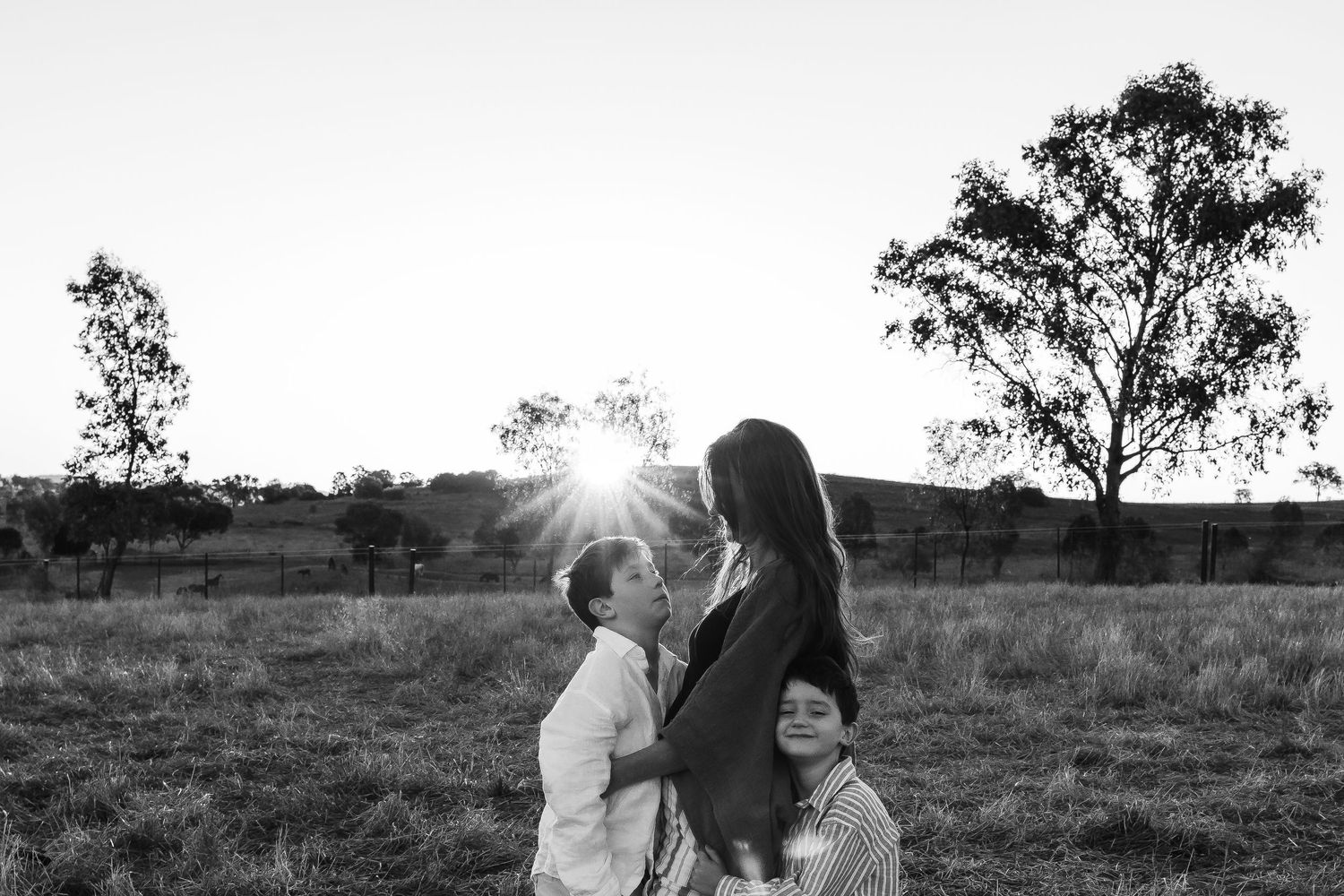 Black and white photo of people in a field at sunset with trees silhouetted against the sky.