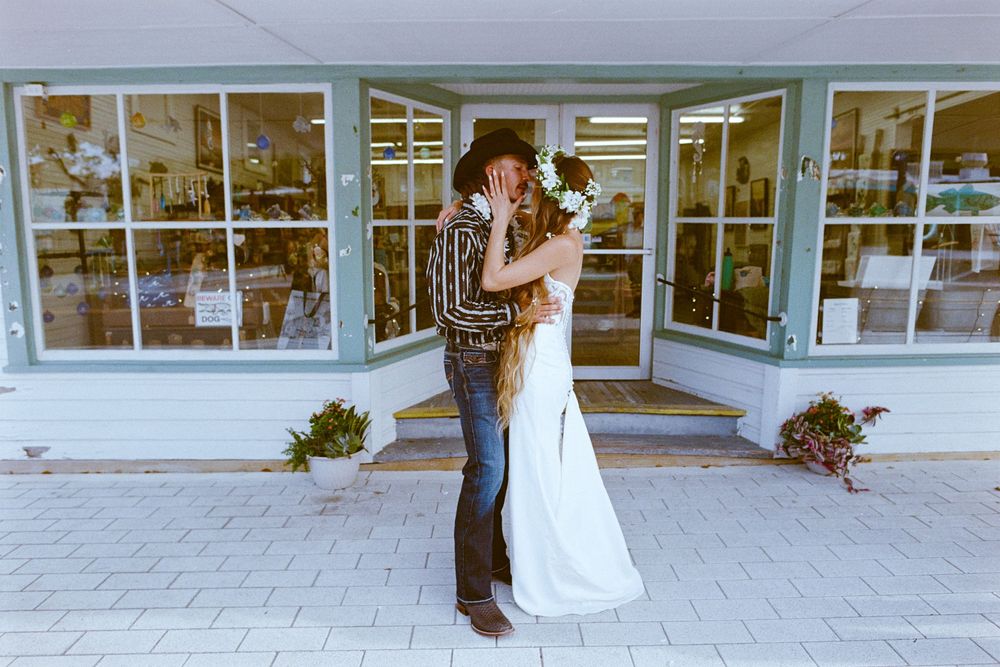 Bride and groom share a kiss in front of a charming storefront on their wedding day.