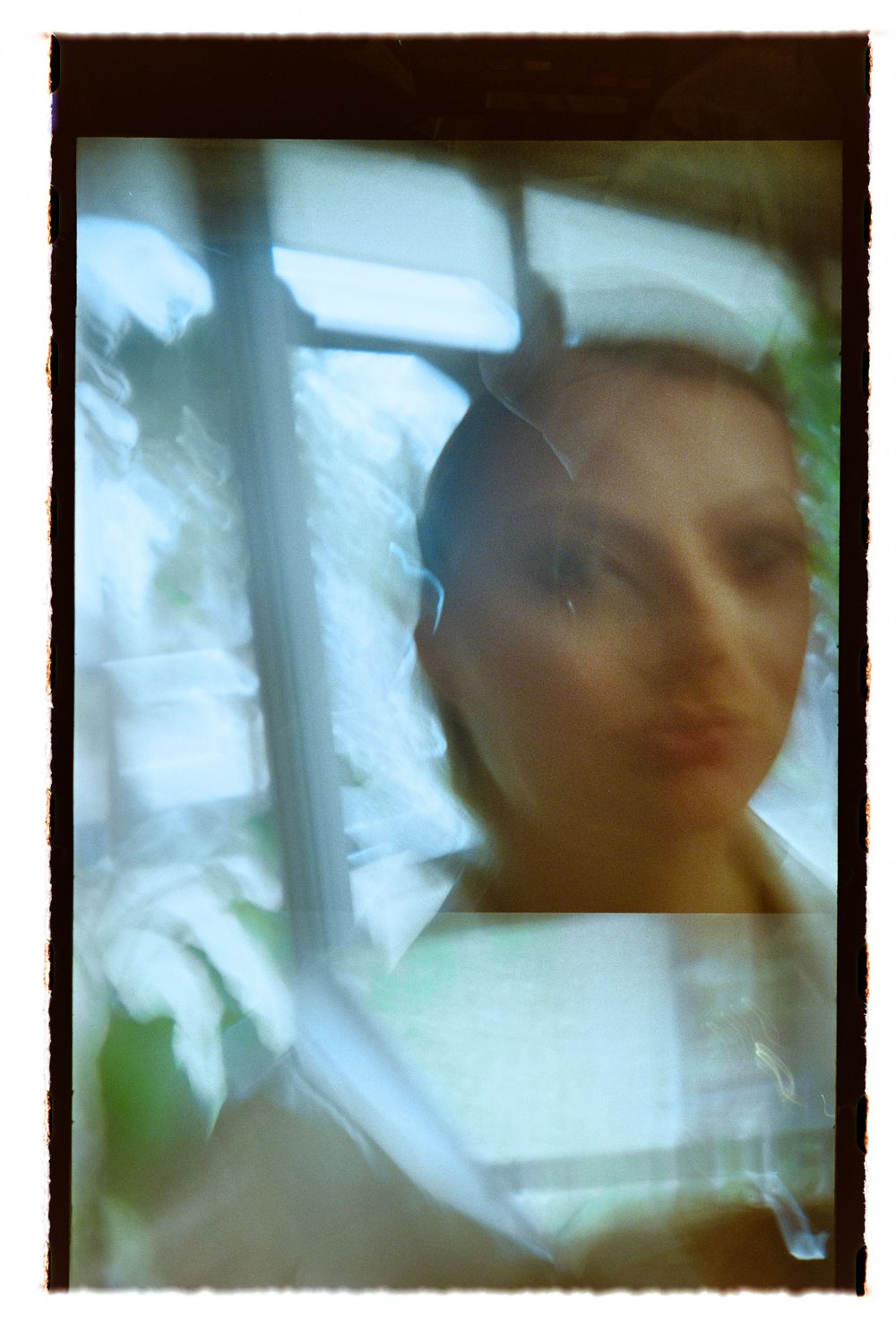 Dreamy double-exposed film portrait of bride reflected through window with soft light.