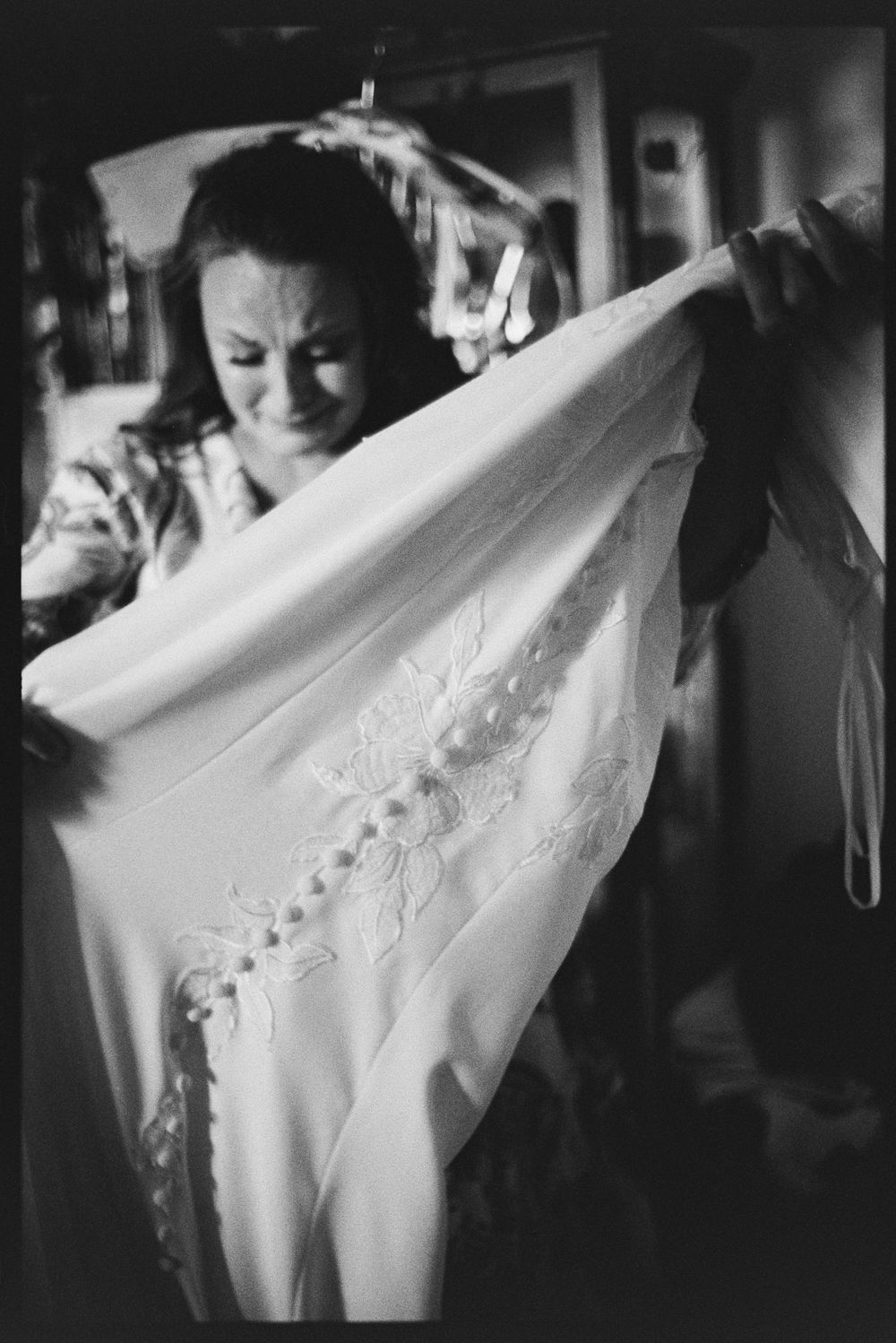 Black and white photo of bride examining lace wedding dress details before ceremony.