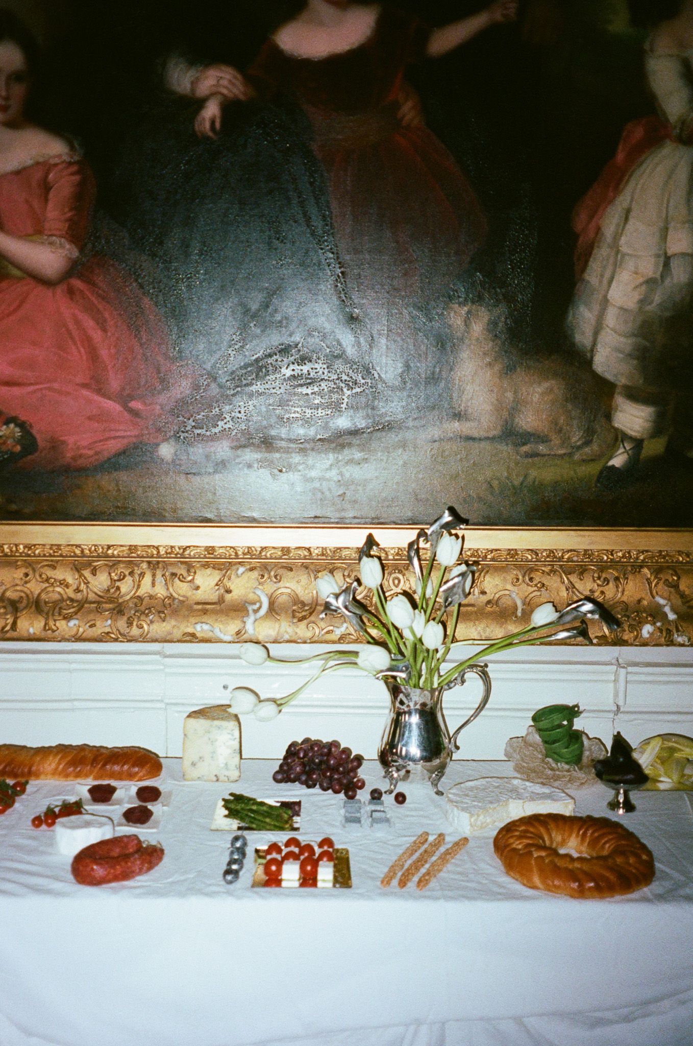 A panoramic view of various appetizers and food items arranged in a line on a white tablecloth against an ornate wall.
