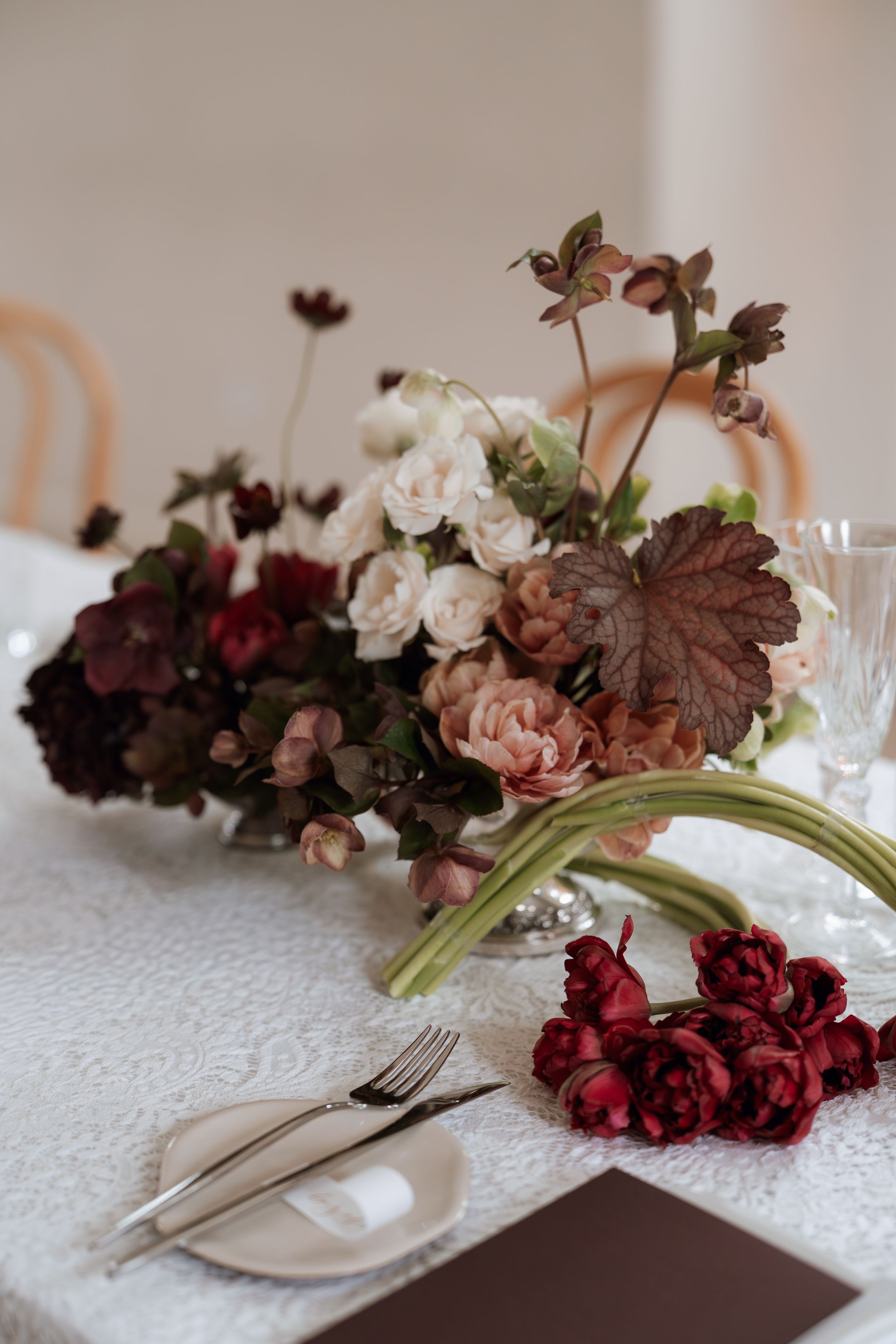 Elegant table setting with burgundy and blush floral arrangements alongside white plates and cutlery on textured linens.