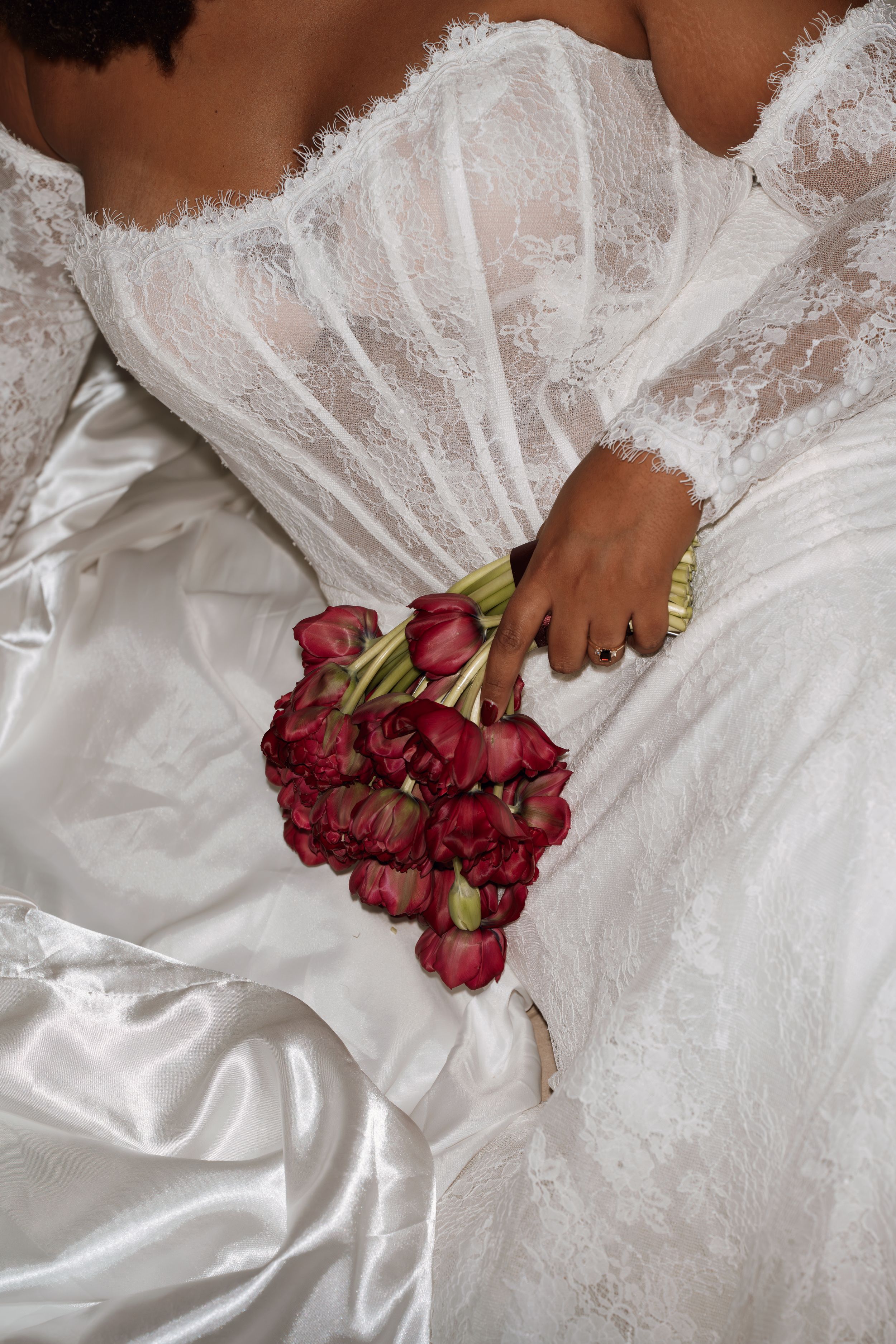 A white lace wedding dress with red roses laying against delicate fabric creating an elegant bridal still life.