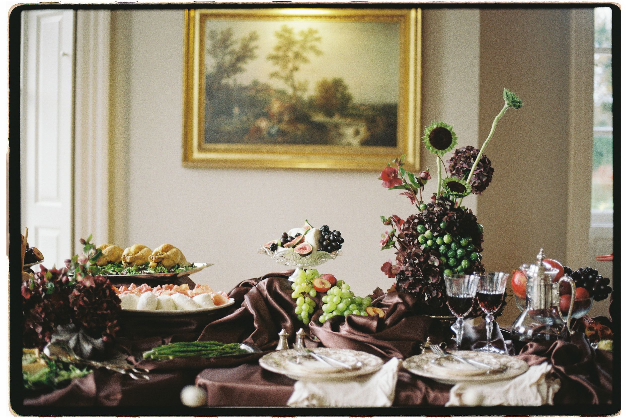 Elegant dining room wall features ornate gold-framed landscape paintings and decorative floral arrangements.