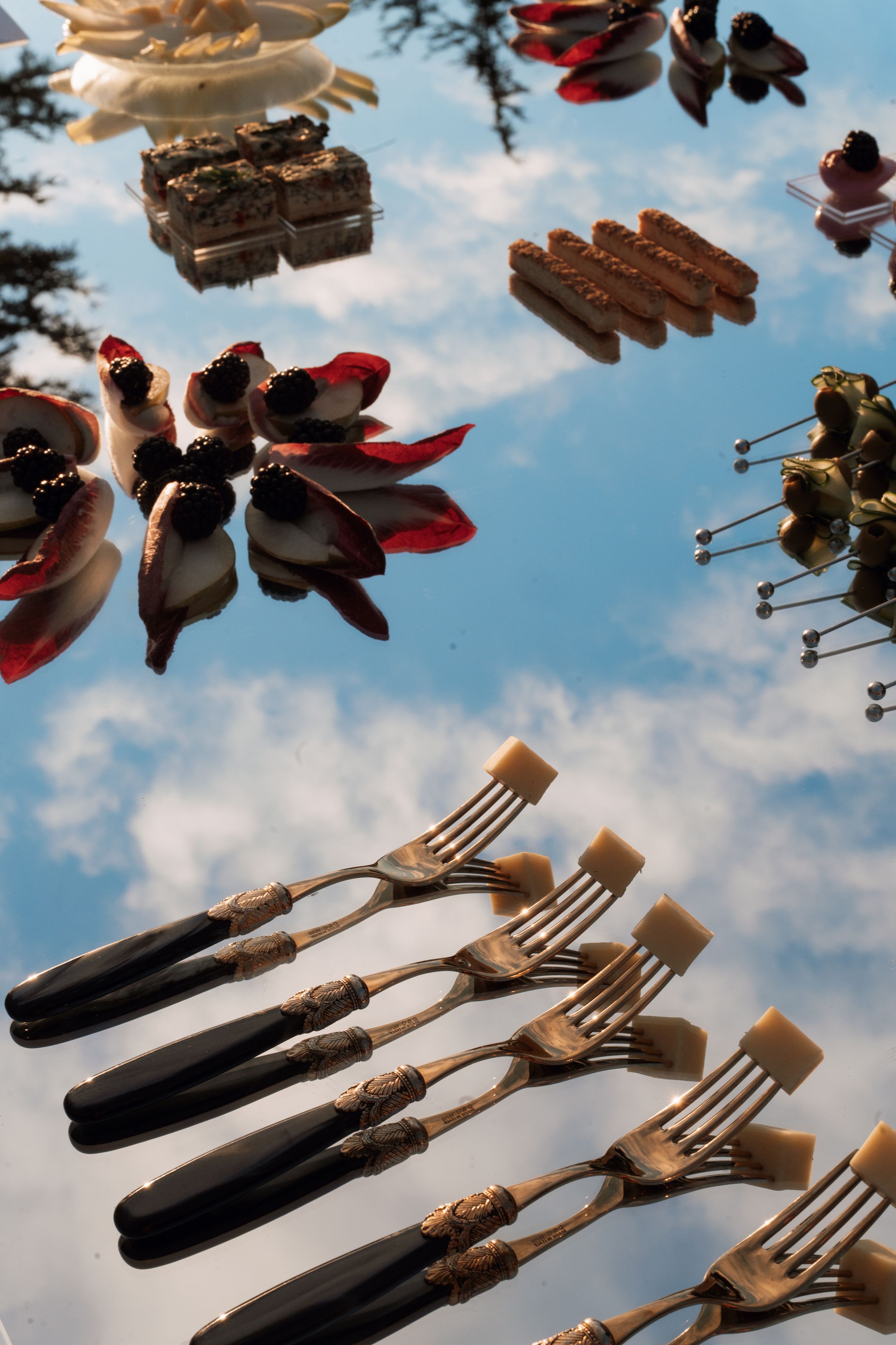 Vintage silverware and utensils floating against a cloudy blue sky background in an artistic arrangement.