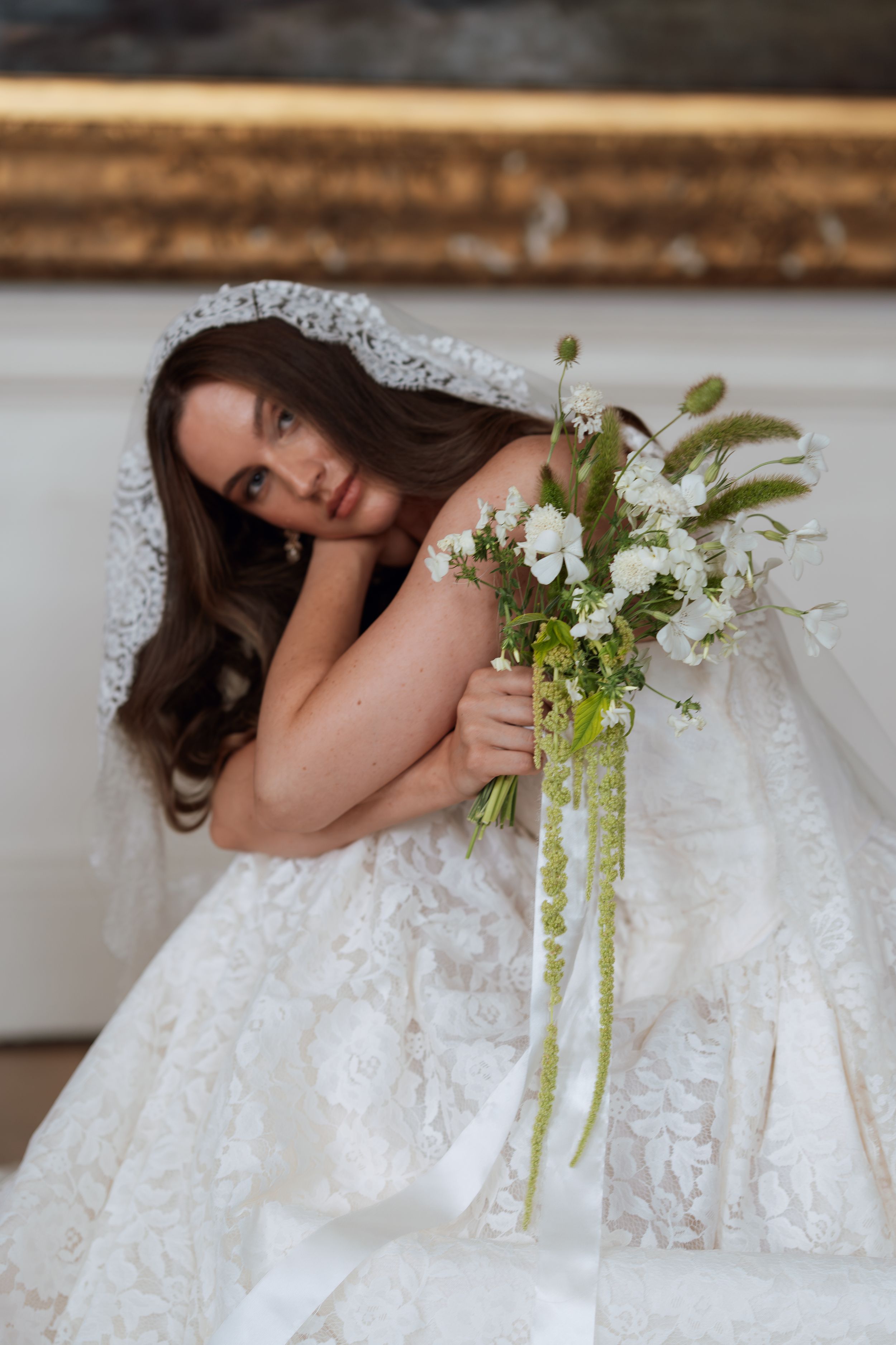 A bride in a white lace wedding dress holds a delicate bouquet of white flowers and greenery.