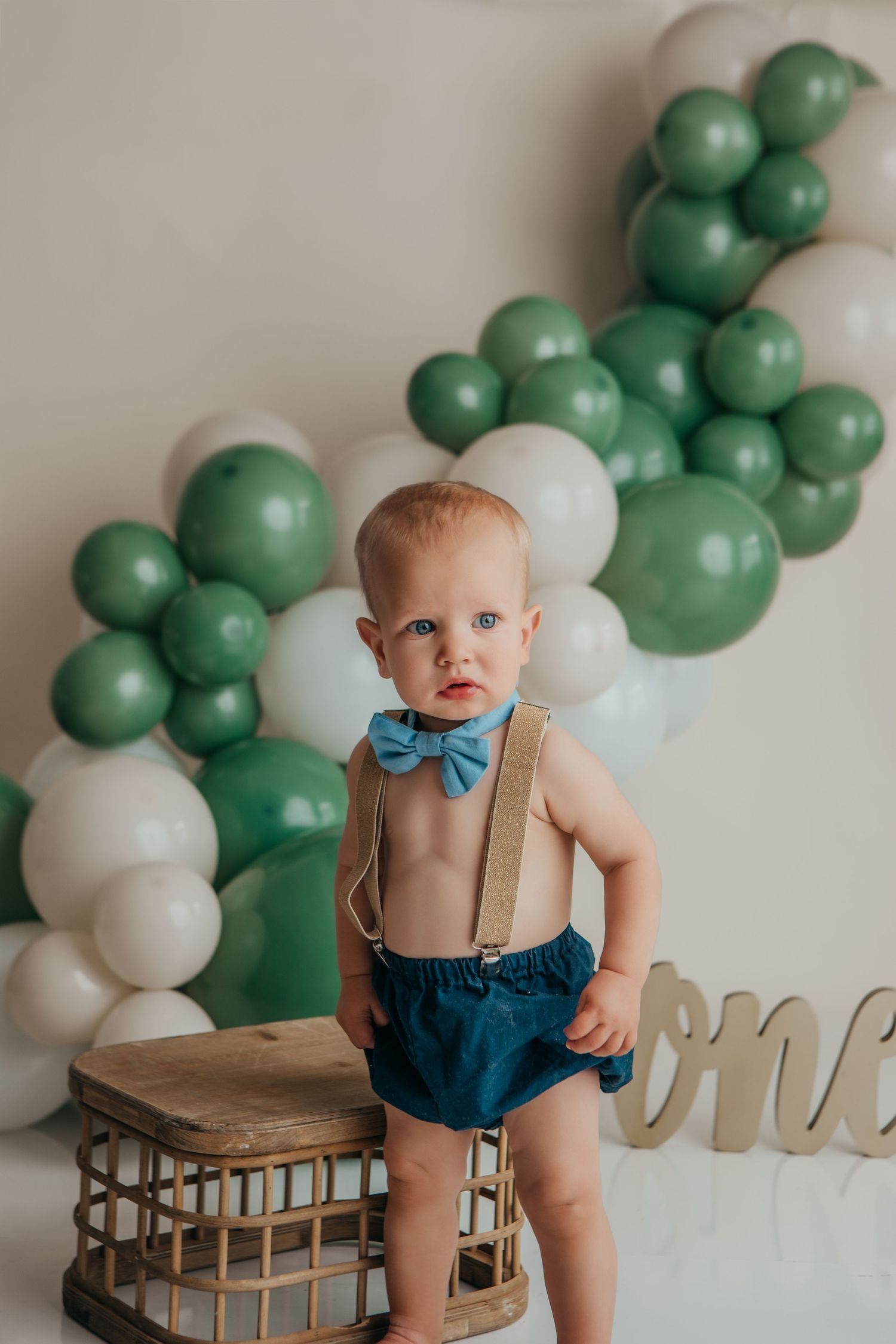 First birthday photo setup with green and white balloons and rustic wooden props.