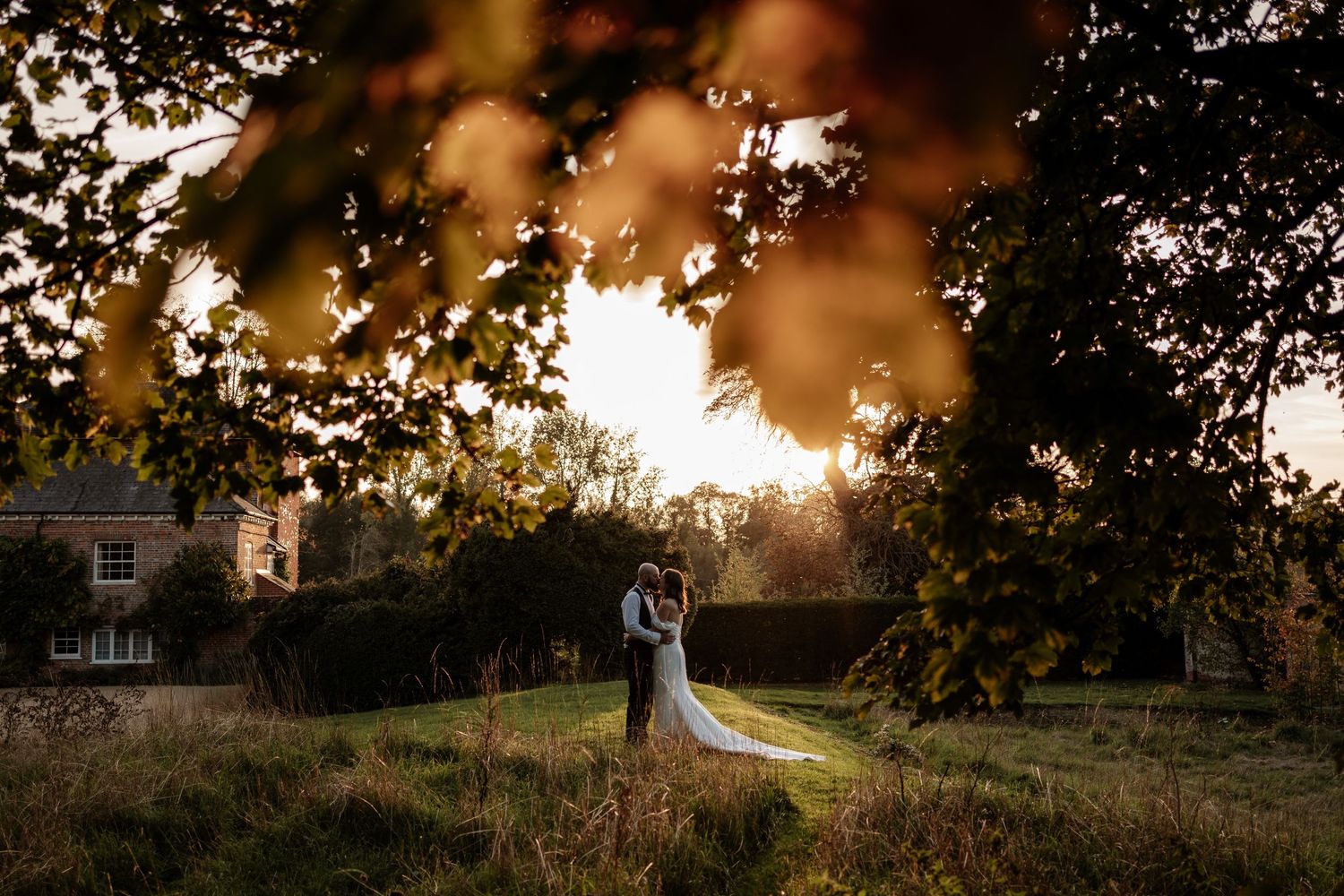A romantic wedding couple poses in golden sunlight during sunset with trees silhouetted in the background.