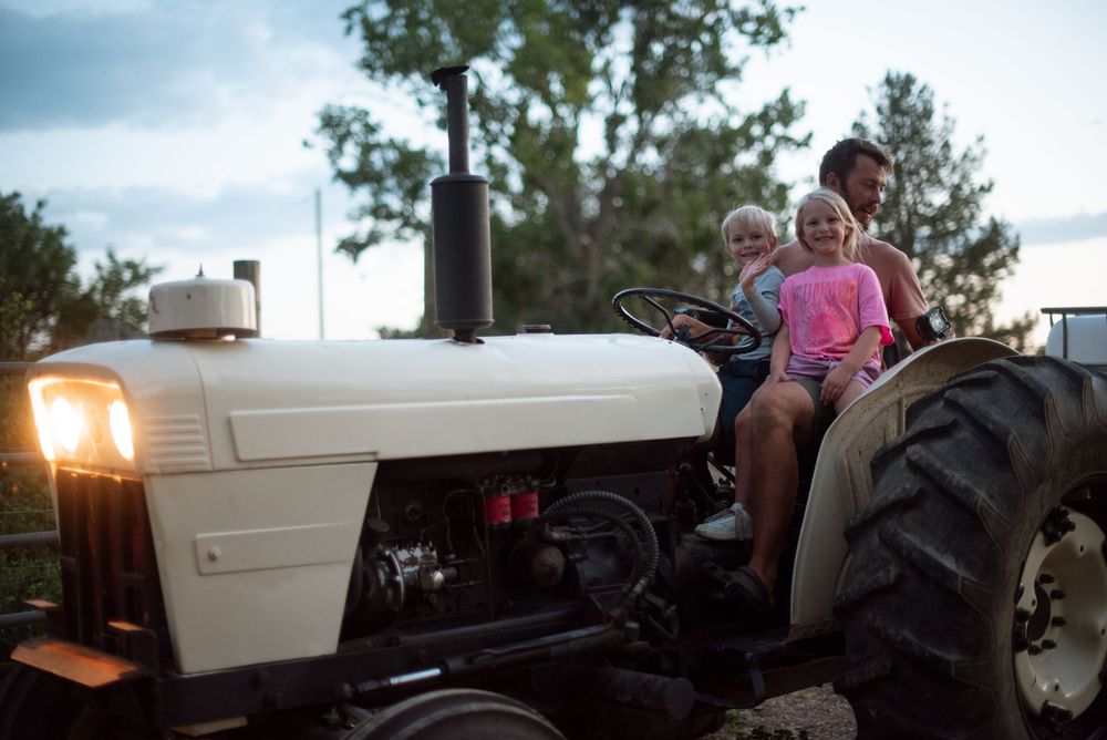 three people riding a tractor at dusk in idaho