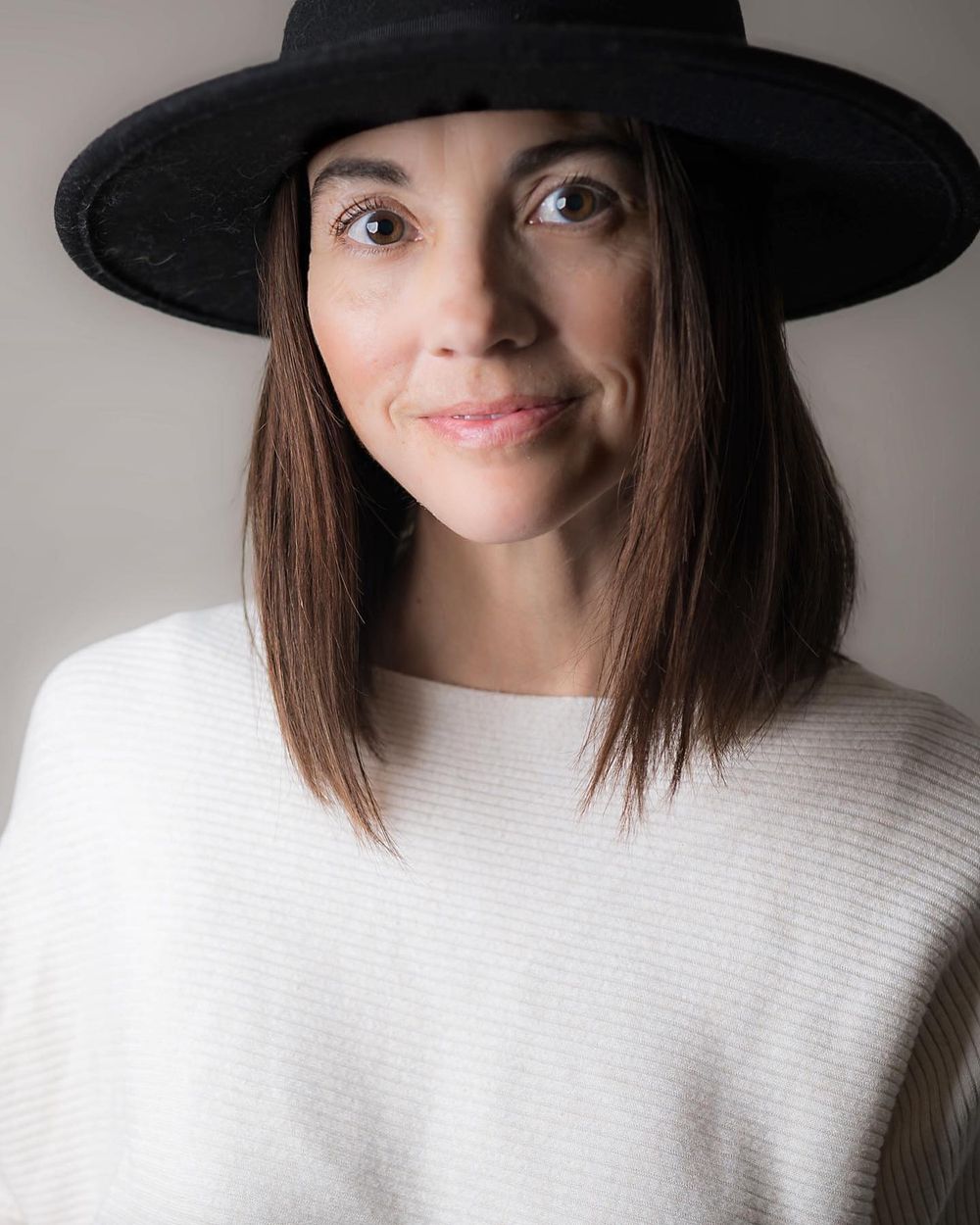 A person in a black wide-brimmed hat and white sweater smiles playfully in a series of expressive portrait shots.