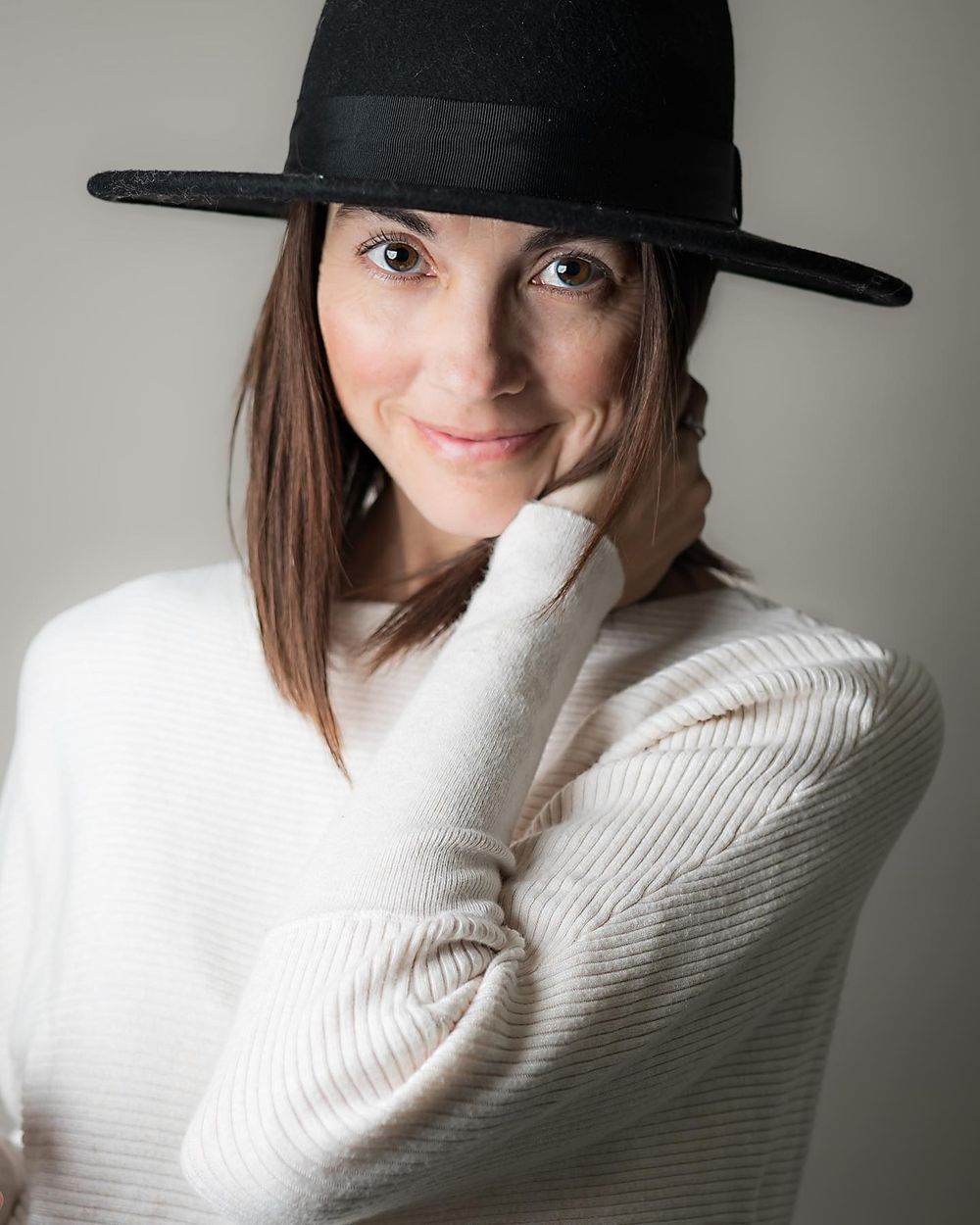 A series of four artistic portraits showing a person in a black hat and white sweater posing against a neutral background.