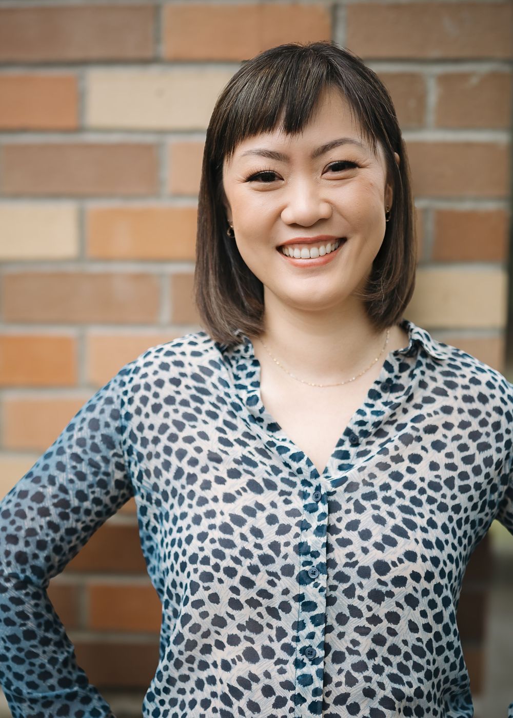 A person wearing a black and white leopard print top poses against a brick wall in a series of expressions.