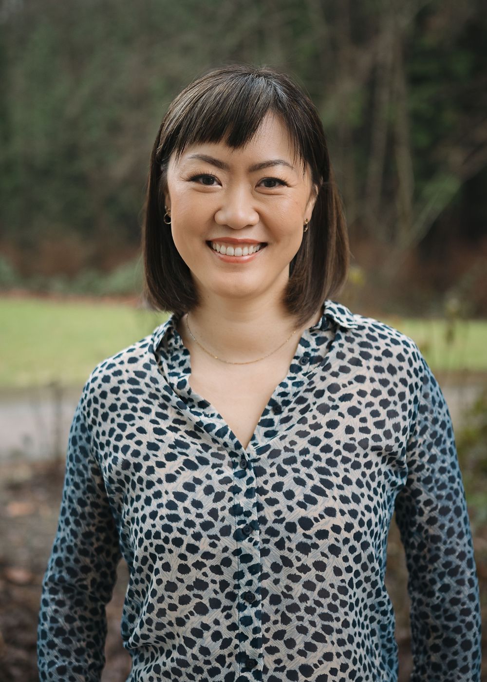 A person in a black and white leopard print top smiles warmly in a series of five similar outdoor portrait shots.