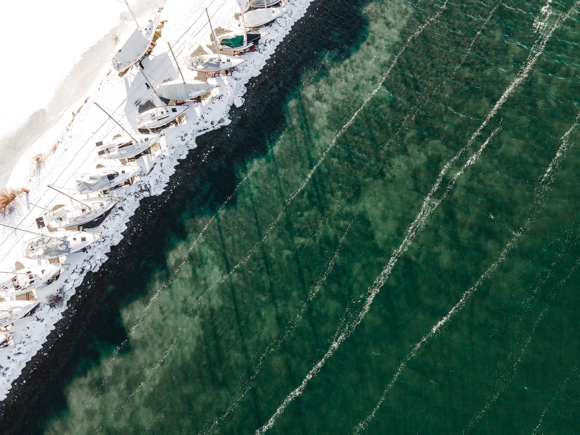 A series of aerial photographs showing a coastal shoreline with dark rocks and green vegetation against blue water. Montreal, Canada. Drone