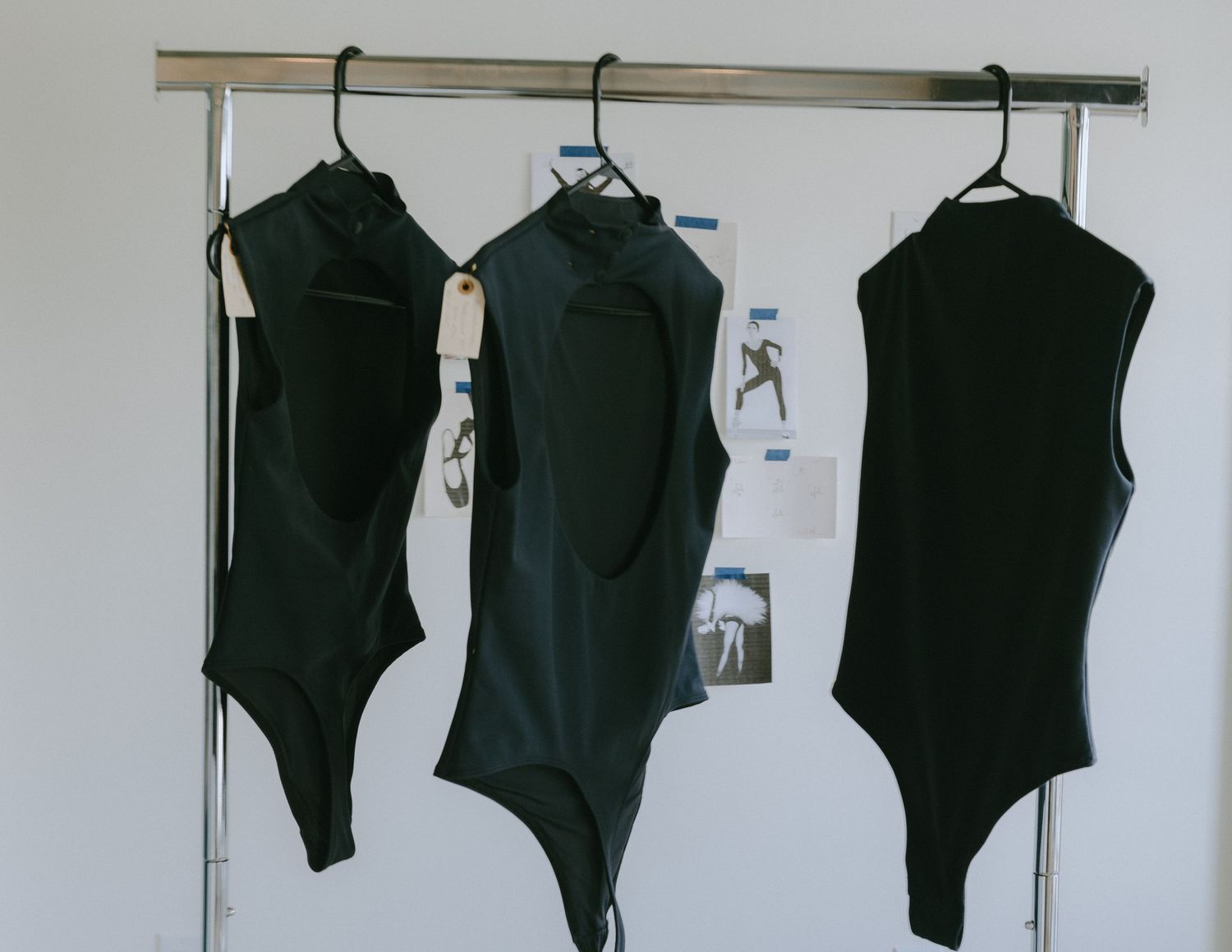 Black garments hanging on a white wall in a row showing a progression of different styles and sizes.