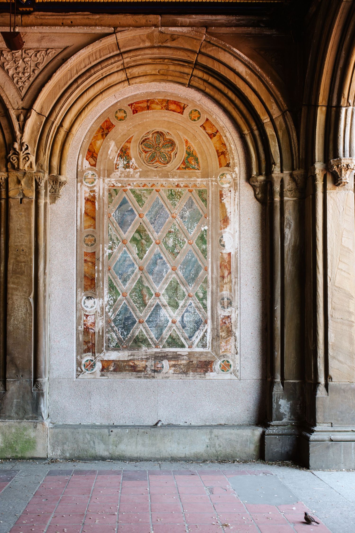 Ornate arched alcove with diamond-patterned stained glass window and decorative stonework in historic architecture.