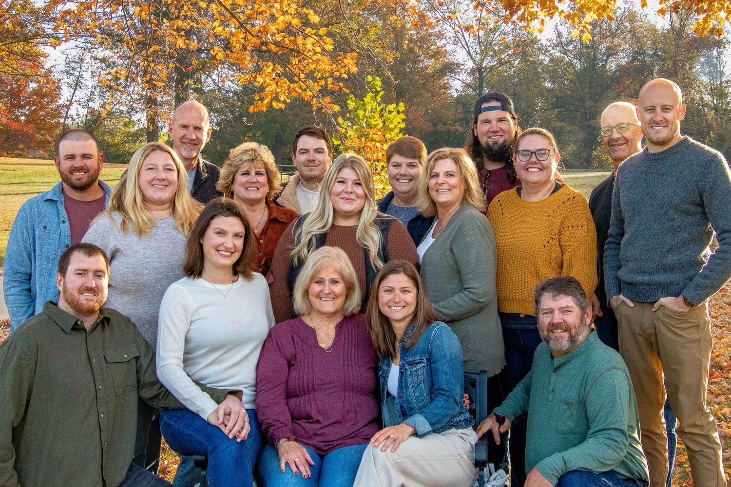 Large family group portrait smiling together outdoors with bright yellow autumn trees behind them.
