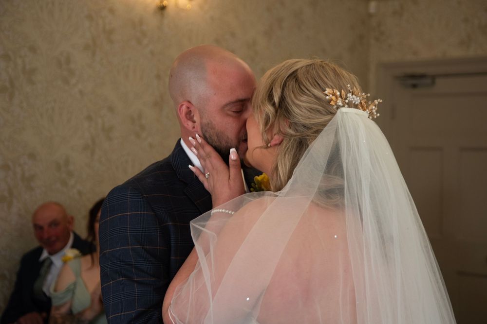 Newlyweds share a tender kiss during their wedding ceremony in an elegant indoor venue.