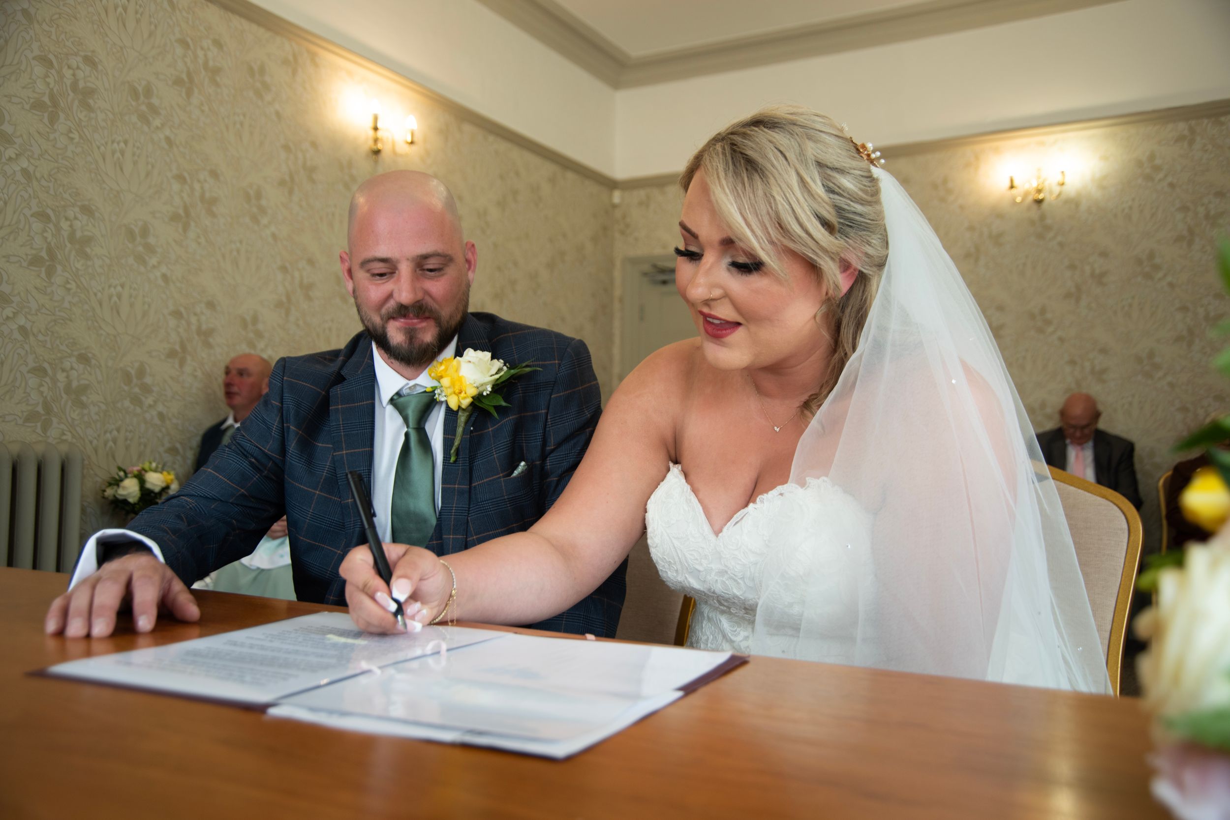 Wedding couple signing their marriage certificate at a registration table with warm lighting.