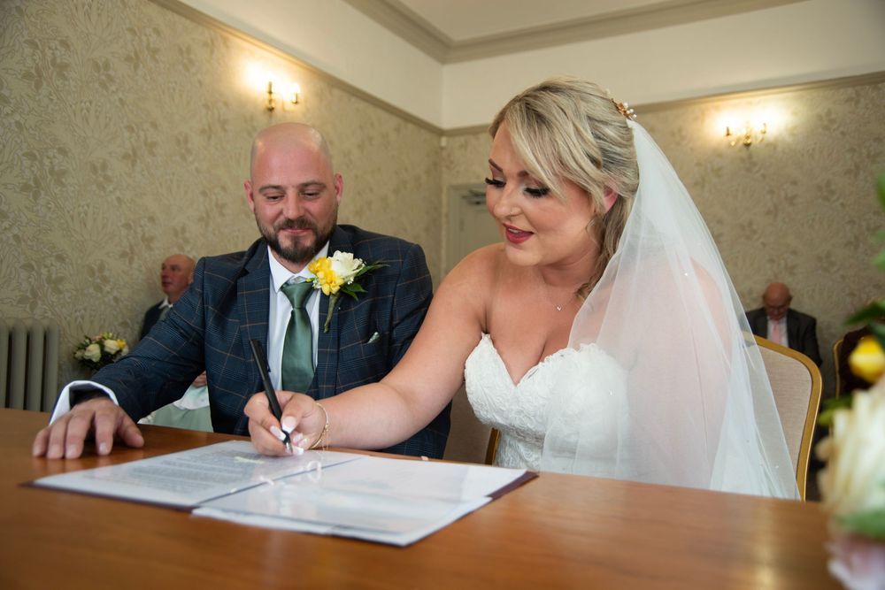 Wedding couple signing their marriage certificate at a registration table with warm lighting.