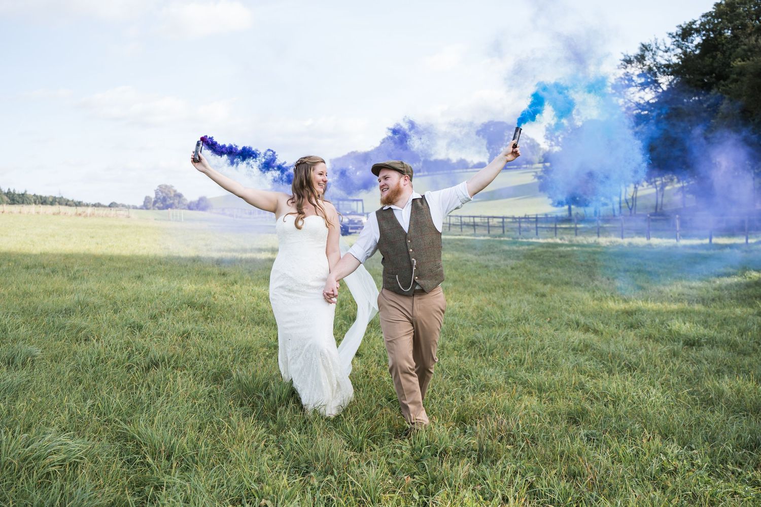 Herons Farm Wedding Photography with Bride & Groom walking through a field with blue and purple smoke