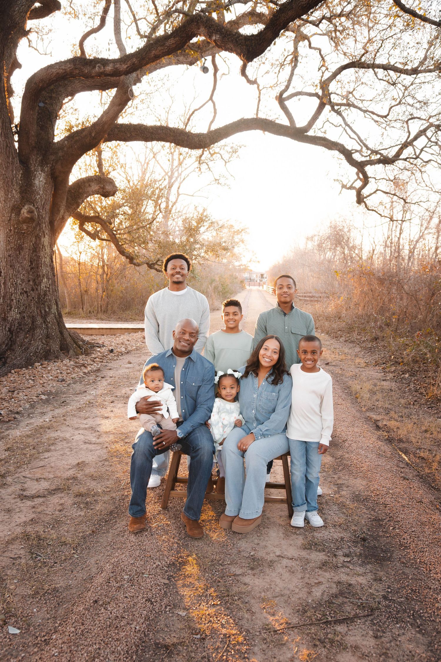 A family wearing coordinated blue and white outfits sits together on a dirt path during golden hour sunset.