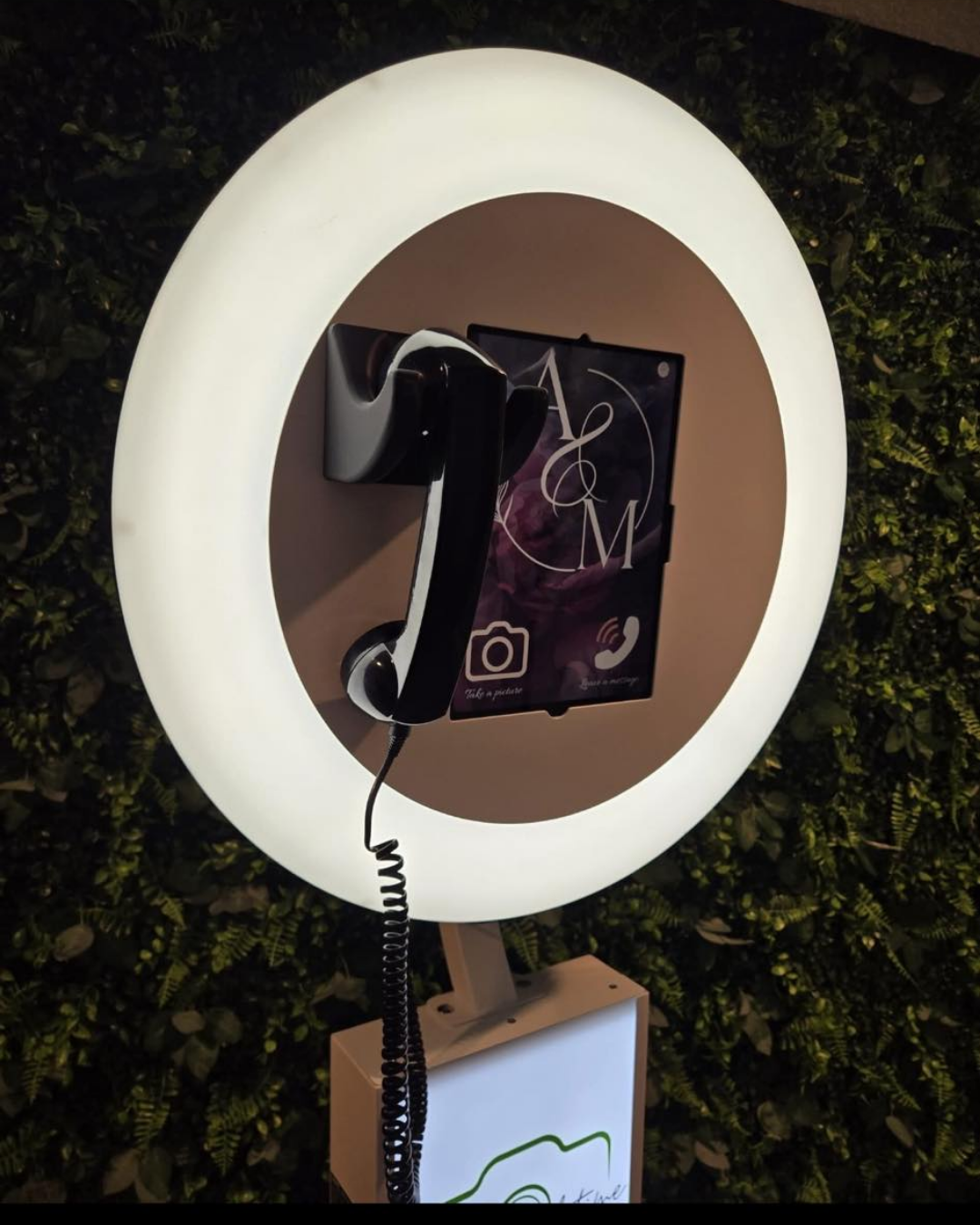 A circular LED ring light with camera mount displays a digital interface screen against a dark leafy background.