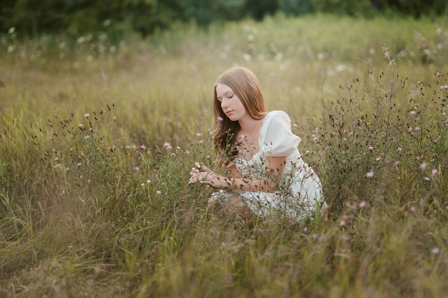 Young woman in white dress sitting peacefully in a wildflower meadow field.