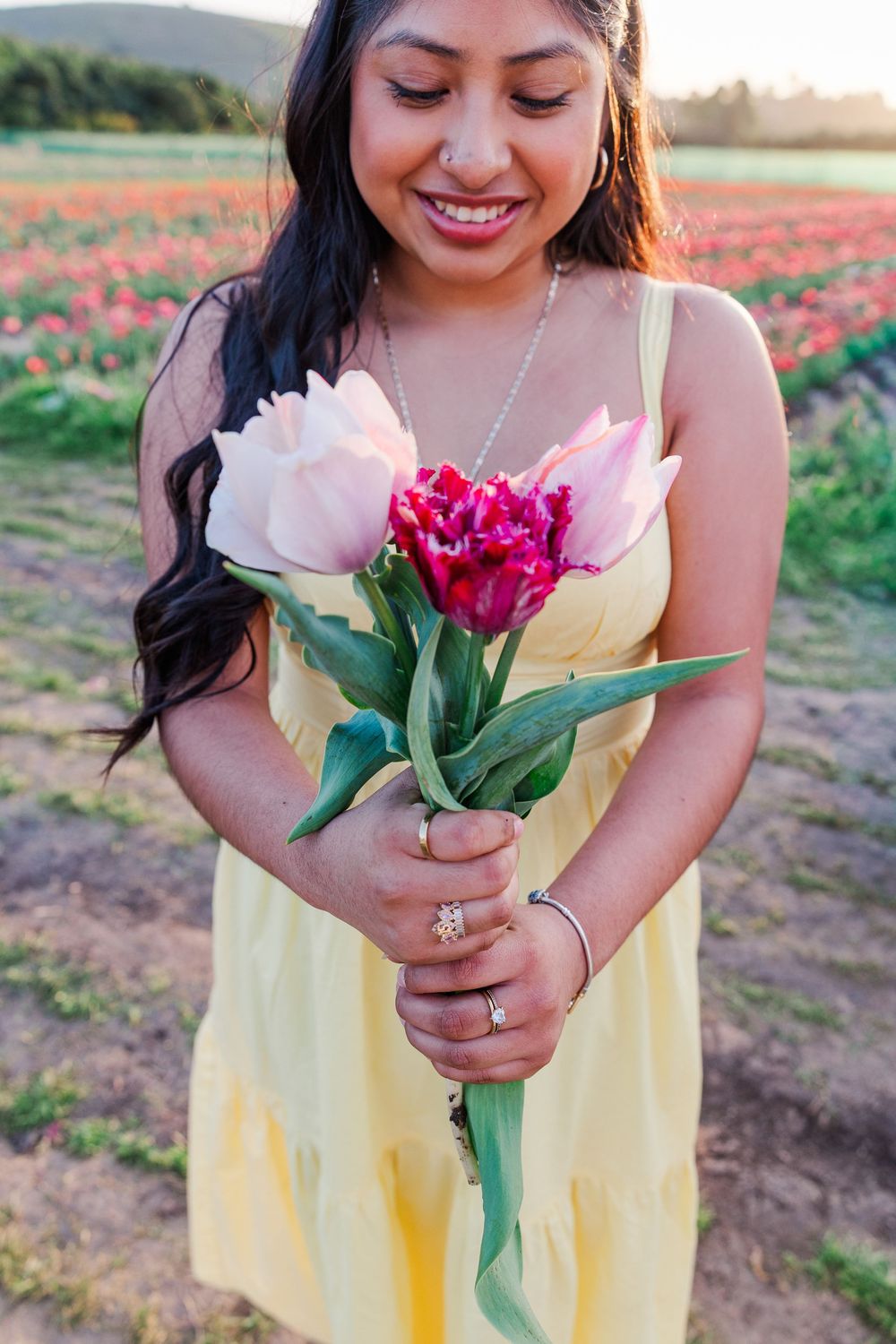 A person in a yellow dress holds vibrant tulips while standing in a blooming spring flower field at sunset.