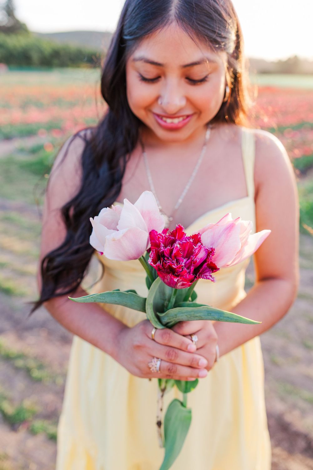 Woman in yellow dress holding pink and red flowers in a sunlit outdoor setting.