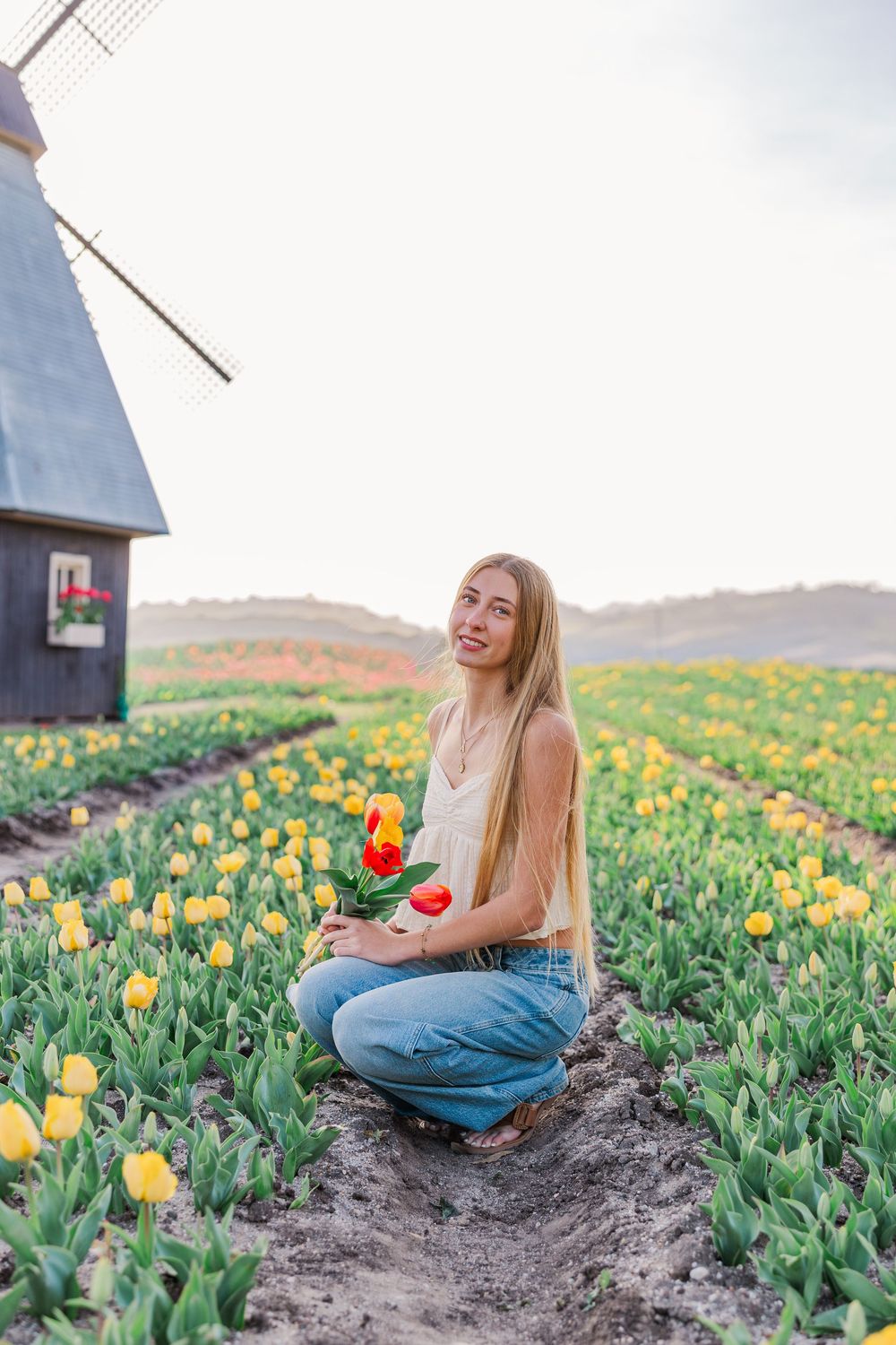 Person sitting among vibrant yellow tulip fields on a spring day with rustic buildings in the background.