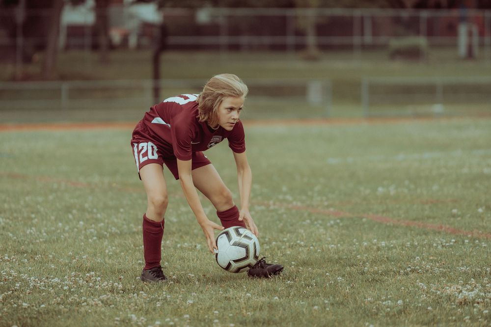 A female soccer player in a maroon number 20 jersey prepares to place the ball on the field.