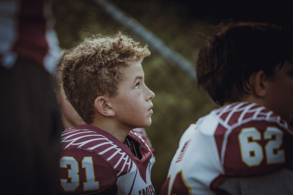A young football player wearing number 31 jersey gazes upward on the sidelines during a game.