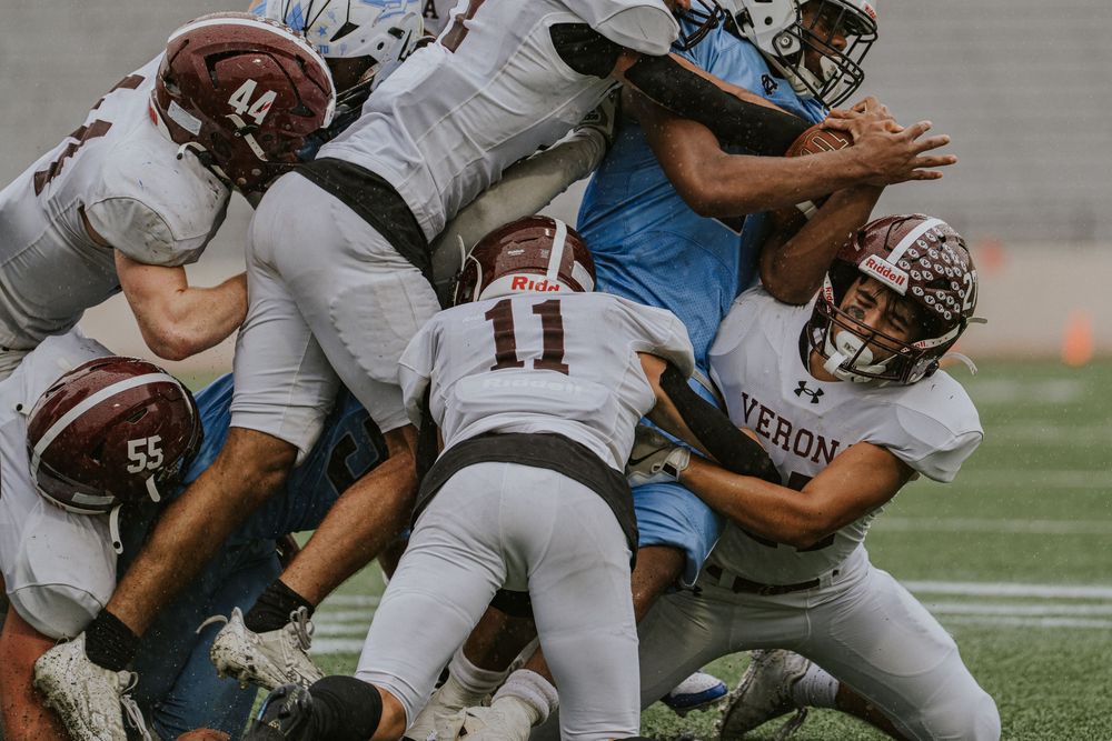 High school football players in maroon Verona jerseys tackling opponent during intense game.