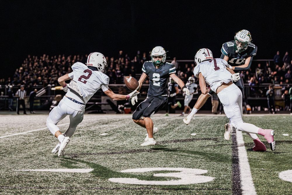 Football players compete during a night game under bright stadium lights on a green field.
