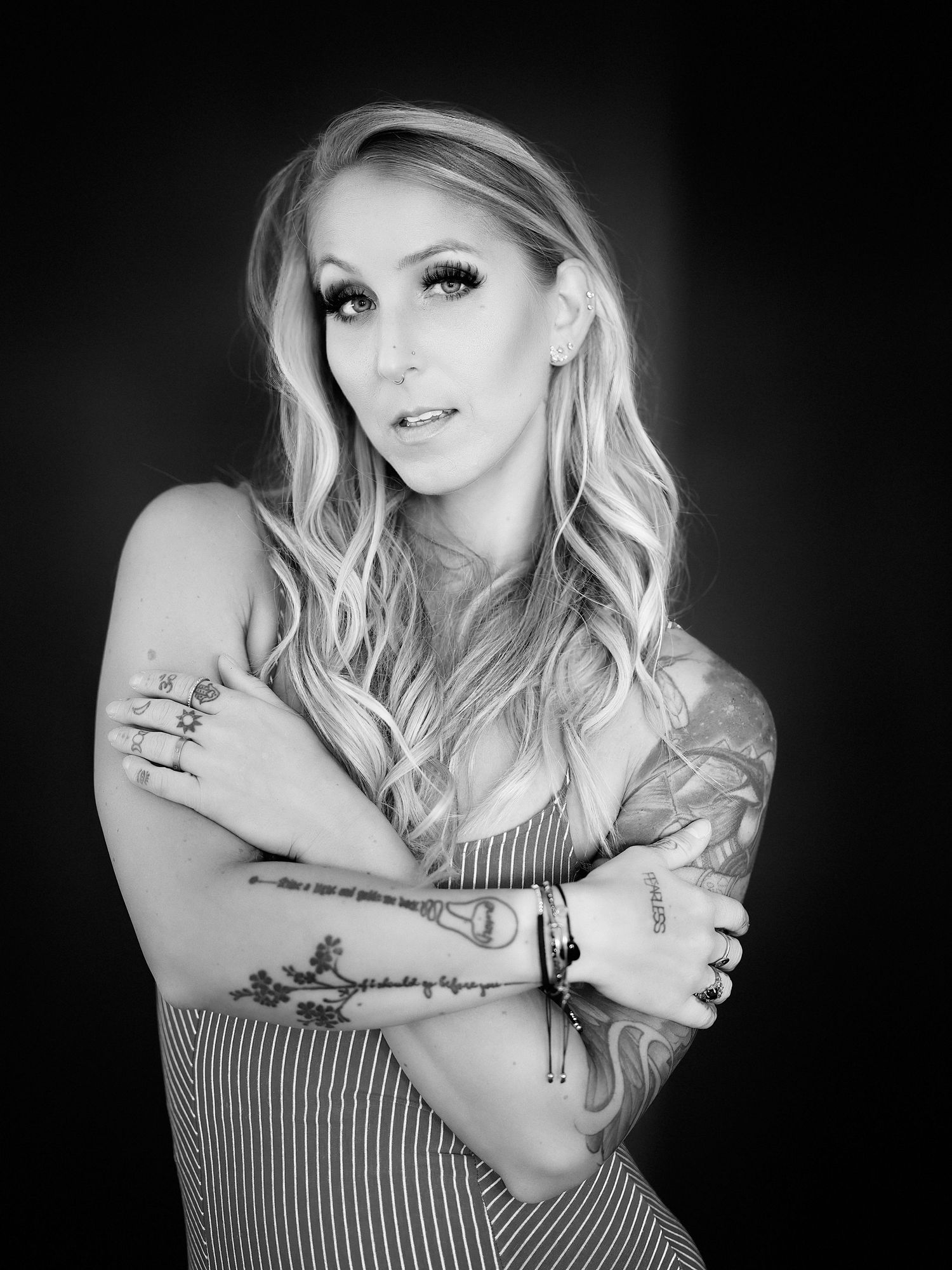 David G Holt Photography - Black and white portrait of a blonde woman with tattoos in a striped top against dark background.