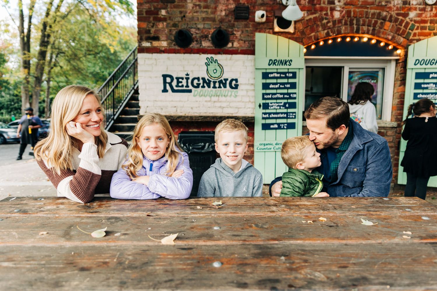 An outdoor scene showing brick walls, foliage and casual gatherings in an urban setting in Charlotte of family photo outside a doughnut shop