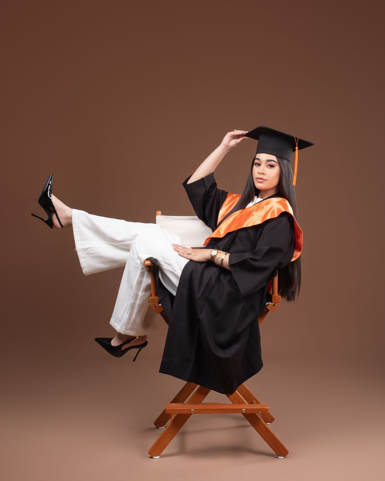 Graduate in black cap and gown holds decorative letters spelling 'GRAD' against peach background.