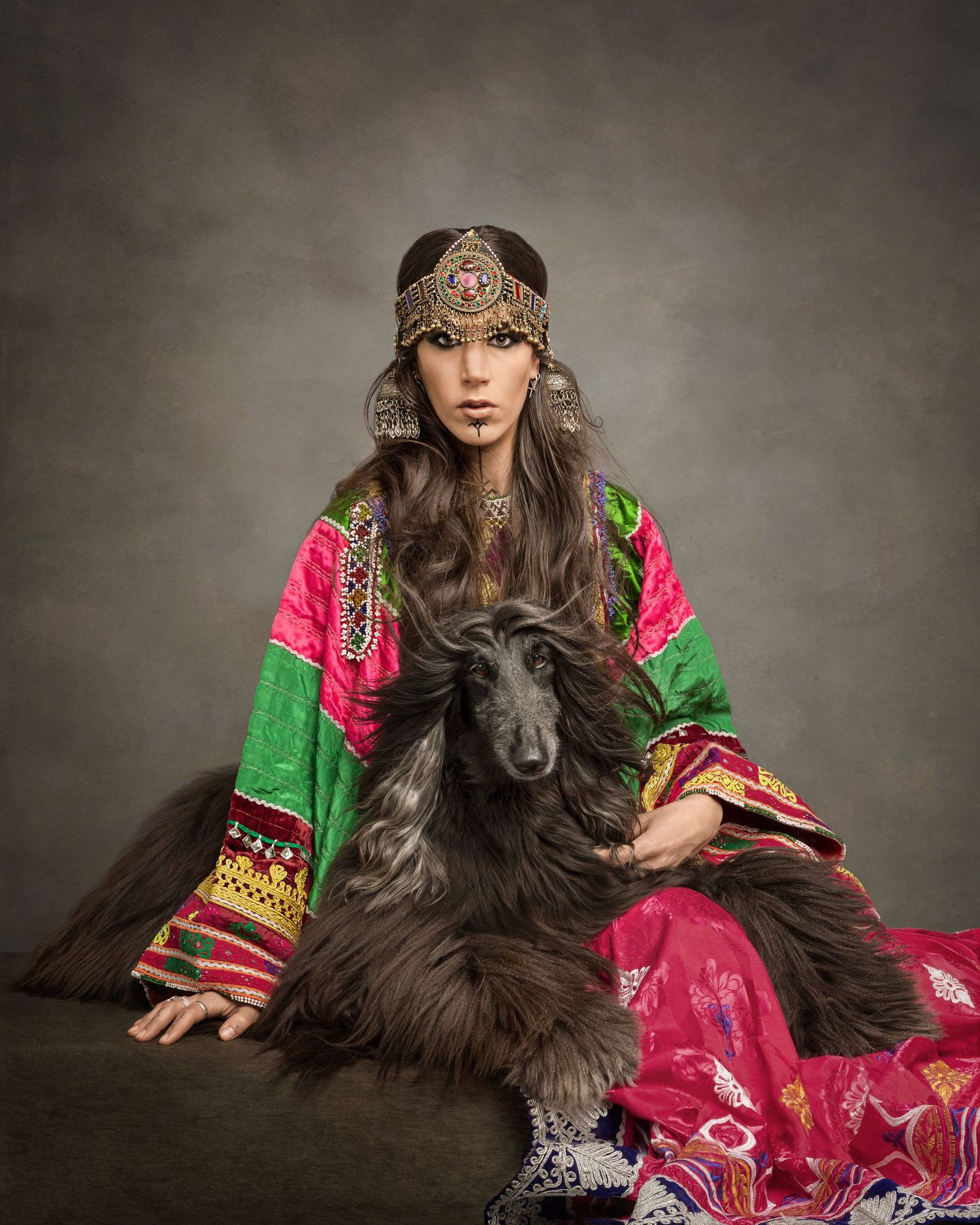 An Afghan dog sitting together with a woman in a traditional Afghan dress in fine art photography